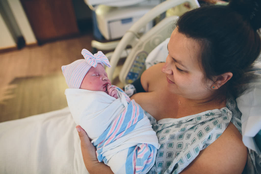 newborn baby girl with bow hat and hospital blanket