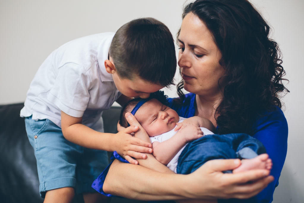 mom holding baby and older brother kissing head