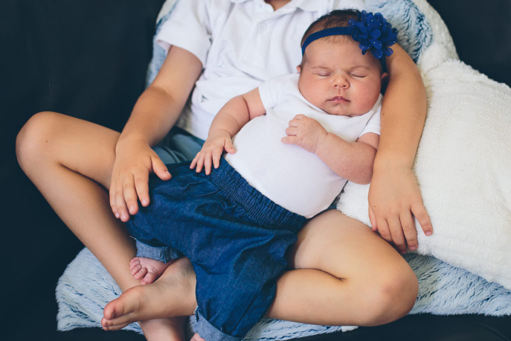 newborn baby sister sleeping on big brother lap