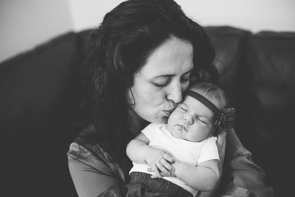 mom kissing newborn baby girl on cheek