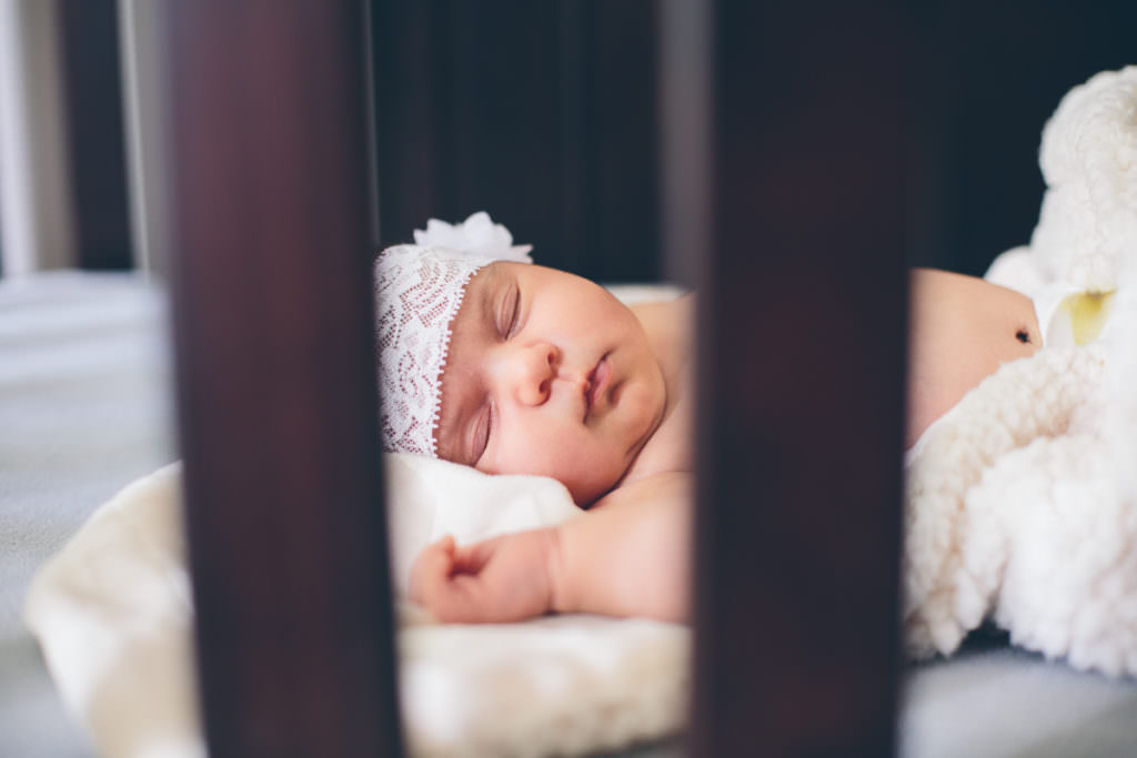 newborn baby girl through slats of her crib