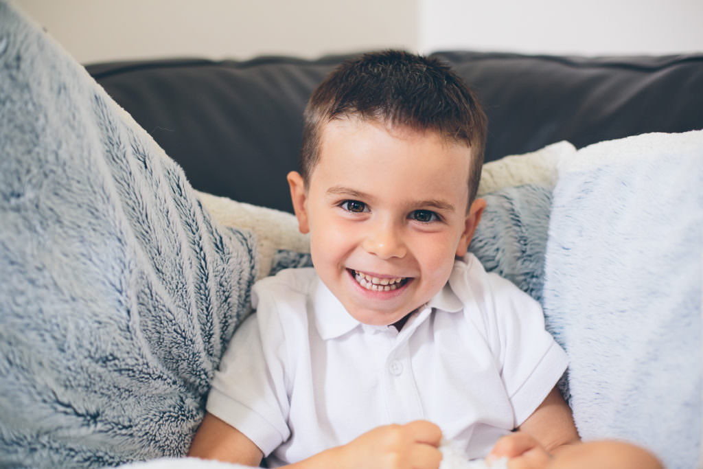 little boy sitting on black couch with white pillows