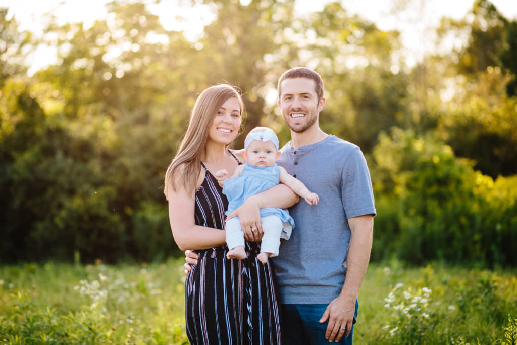 mom and dad holding baby in field