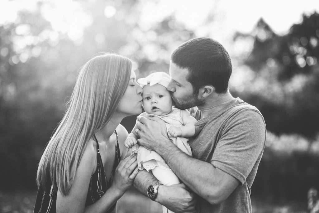 mom and dad kissing baby on cheek