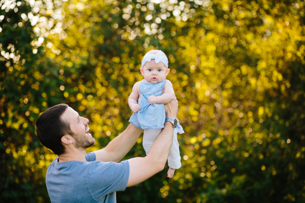 baby girl in blue dress by green tree