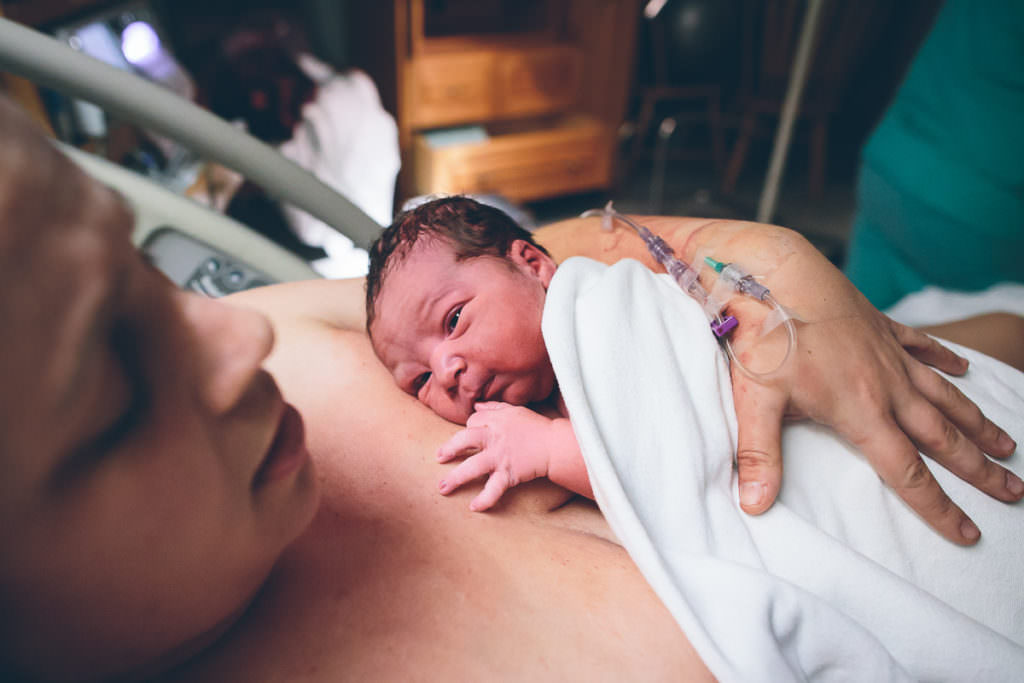 newborn baby boy laying on moms chest under white blanket after his birth