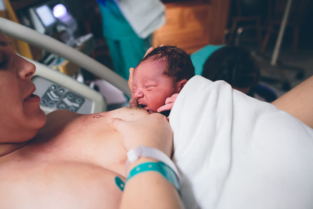 mom holding breast and offering nipple to newborn baby boy