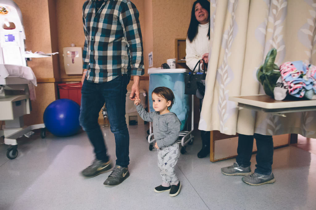 dad holding big brothers hand as he comes to meet his new baby brother