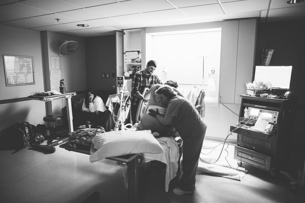 hospital room mom laboring on bed with husband and nurse support mom sitting in corner