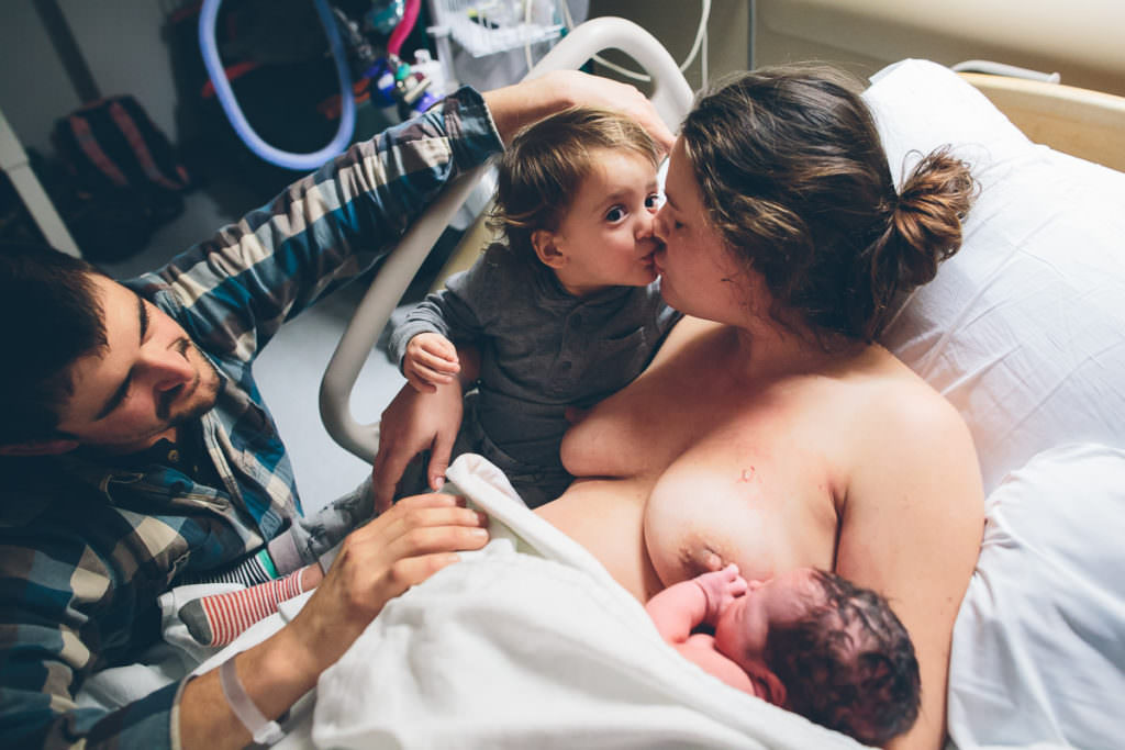 toddler giving mom a kiss after he meets his new brother at the hospital