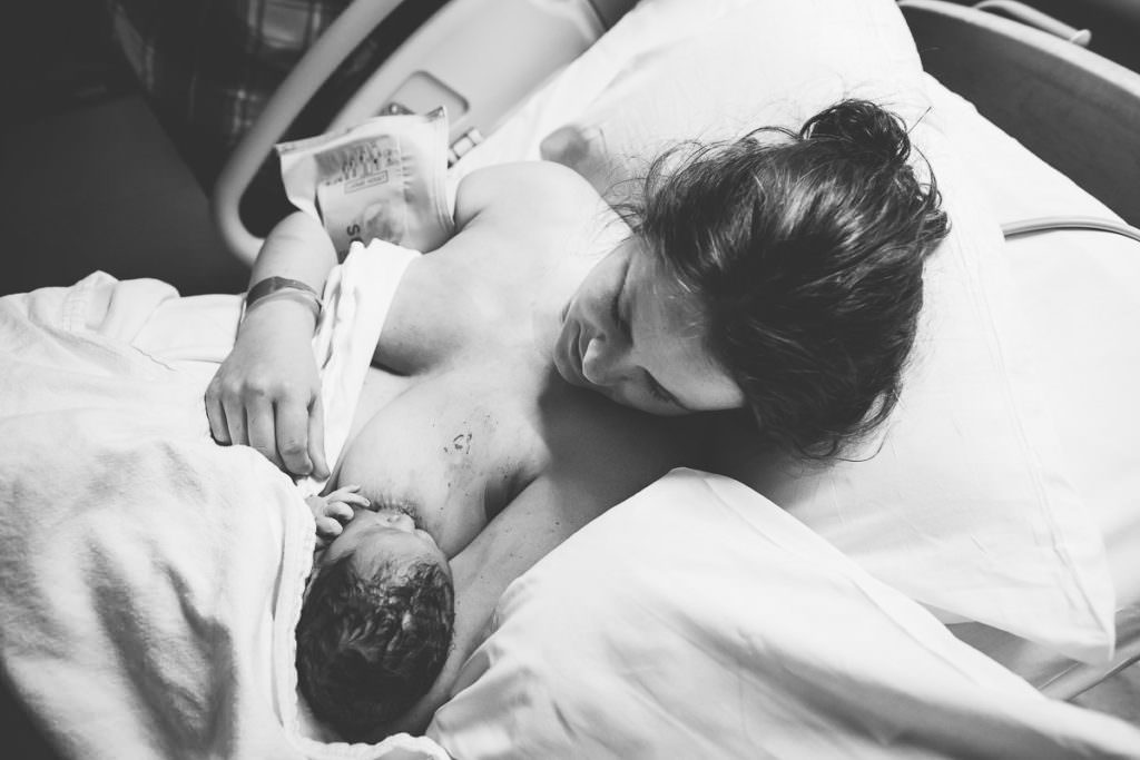 mom looking at her newborn after he latches while breastfeeding