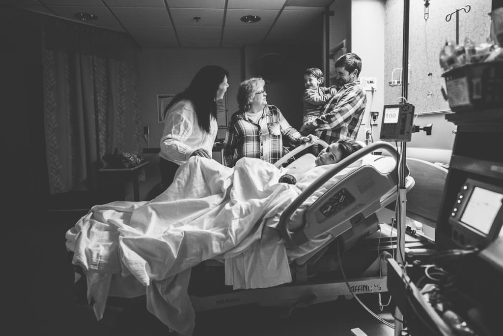 guests standing around hospital bed after mom delivers a baby boy