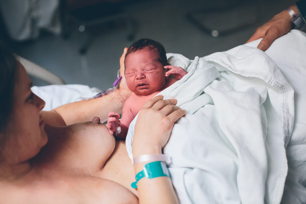 mom un wrapping newborn baby boy to nurse on the other side