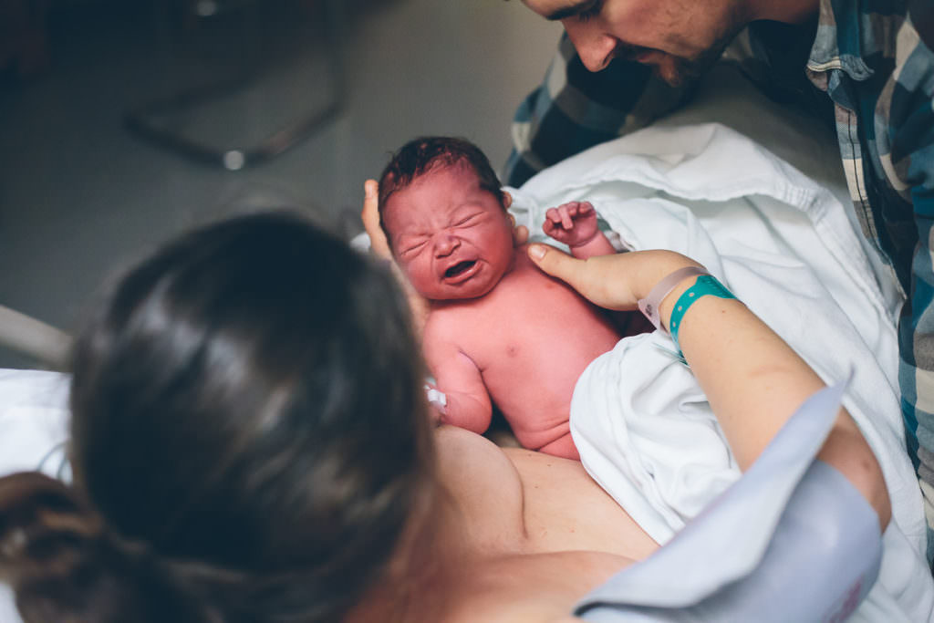 mom checking out her newborn baby boy with dark hair and rosy skin