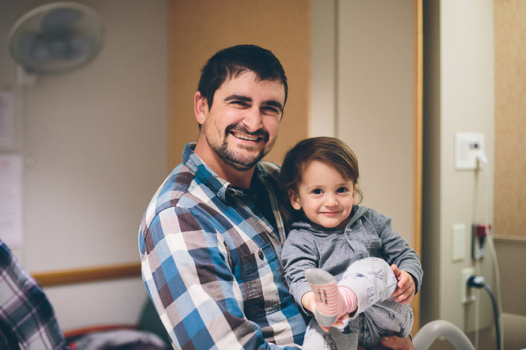 dad holds toddler while visiting mom and new baby at the hosptial