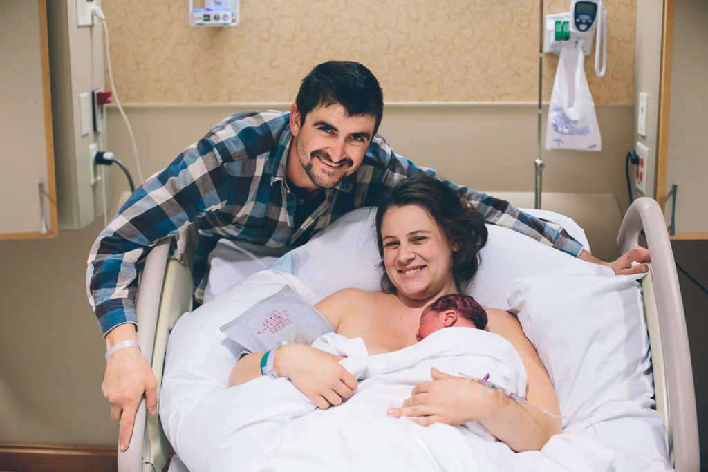 mom dad and baby posing for picture on hosptial bed