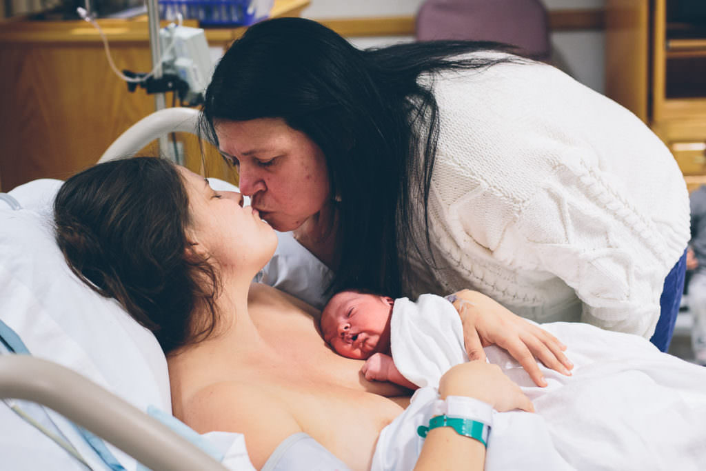 mom gives daughter a kiss after seeing her give birth to her grandson