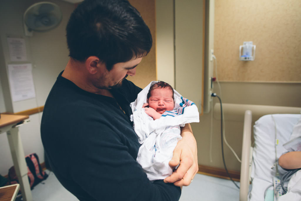 dad holds baby wrapped in a hospital blanket
