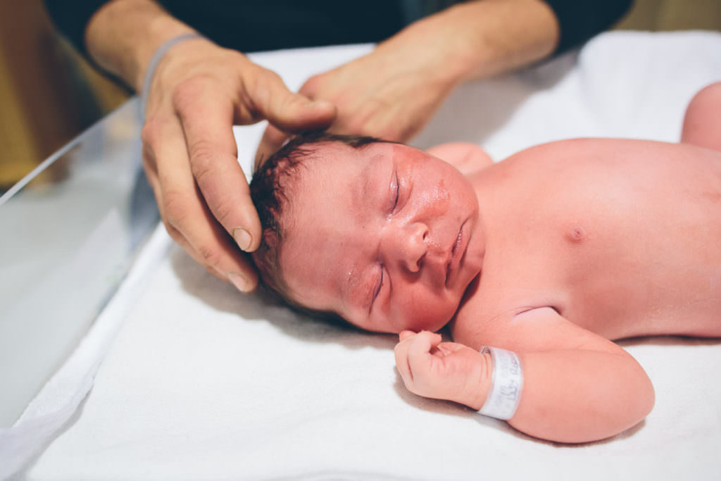 father holds new baby head while getting newborn exam