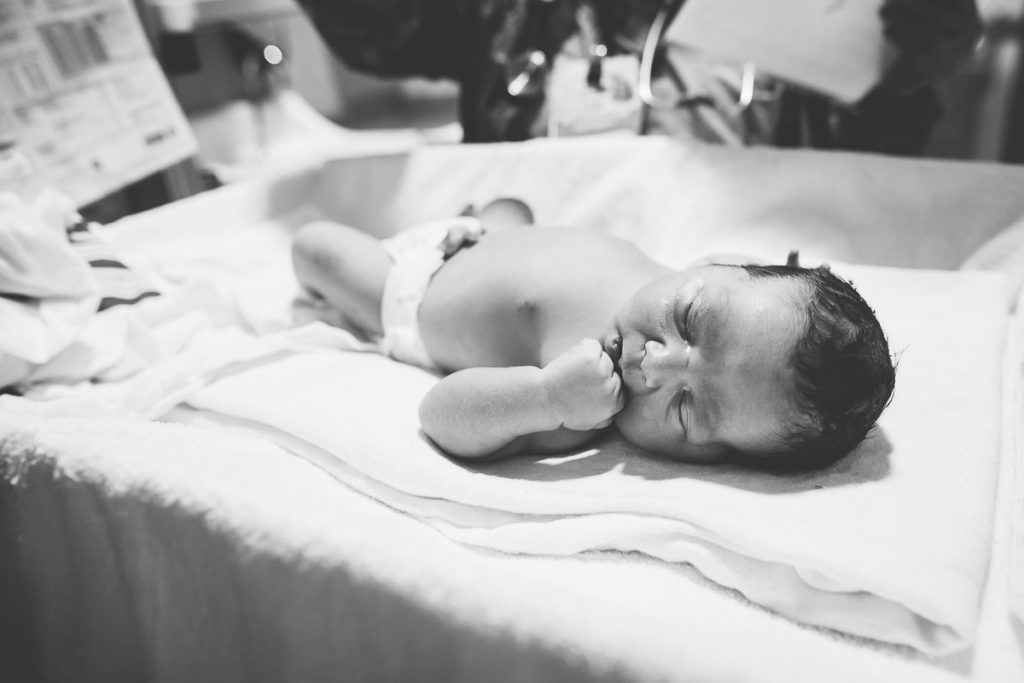 newborn baby boy with fist to his mouth and wearing a diaper