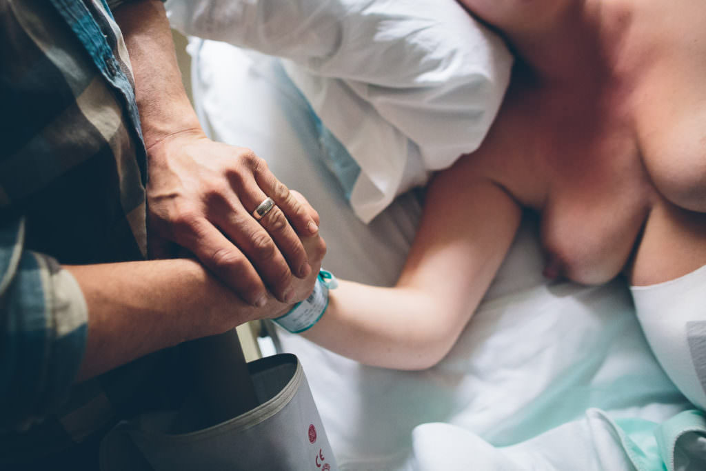 close up of dad holding his wife hands while she gives birth