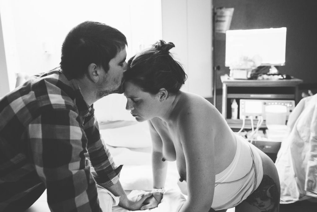 dad kisses mom on forehead while she rests between contractions