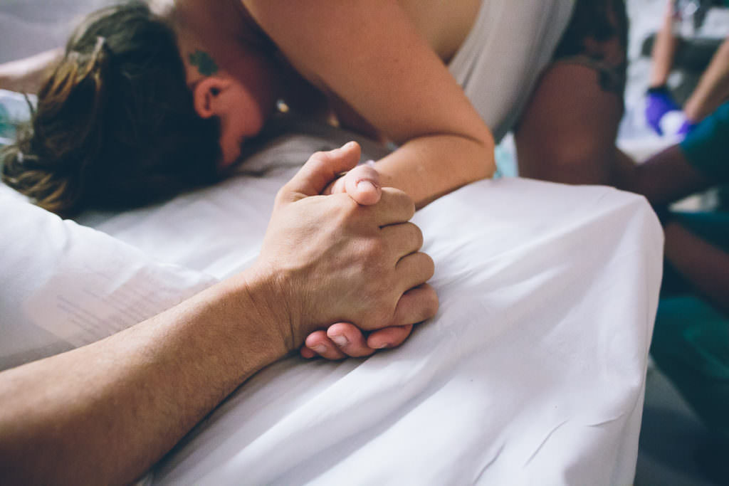 husband and wife holding hands over hospital bed