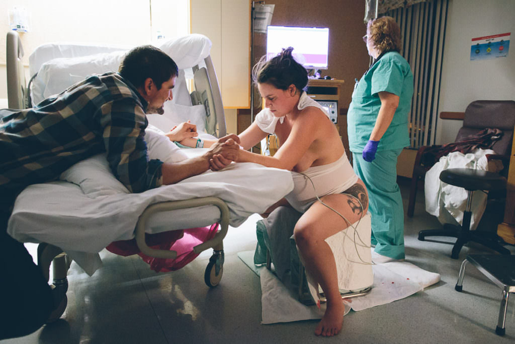 mom sits on birthing stool next to bed during her vbac low intervention hospital birth