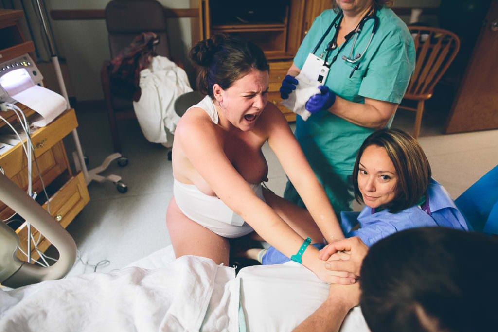 mom screams during strong contraction on birth stool midwife down below smiling up saying baby is coming