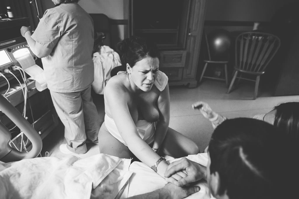 mom reaches down on birthing stool during vbac to feel baby's head