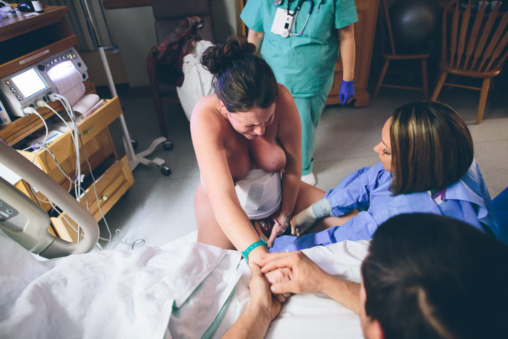 mom reaches down while crowning on birthing stool during vbac