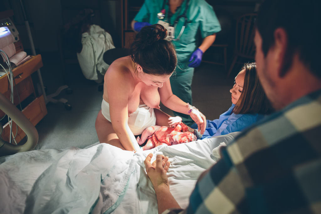 midwife brings up baby that was just born on birth stool to moms arms