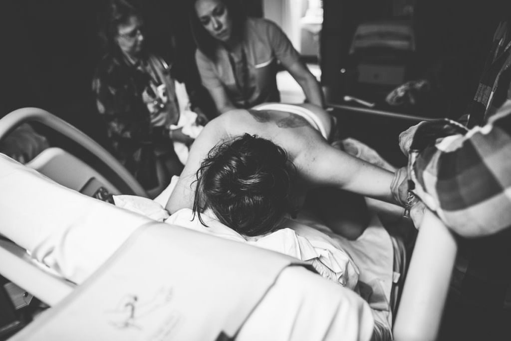 black and white image of mom laboring on all fours head facing the back of bed