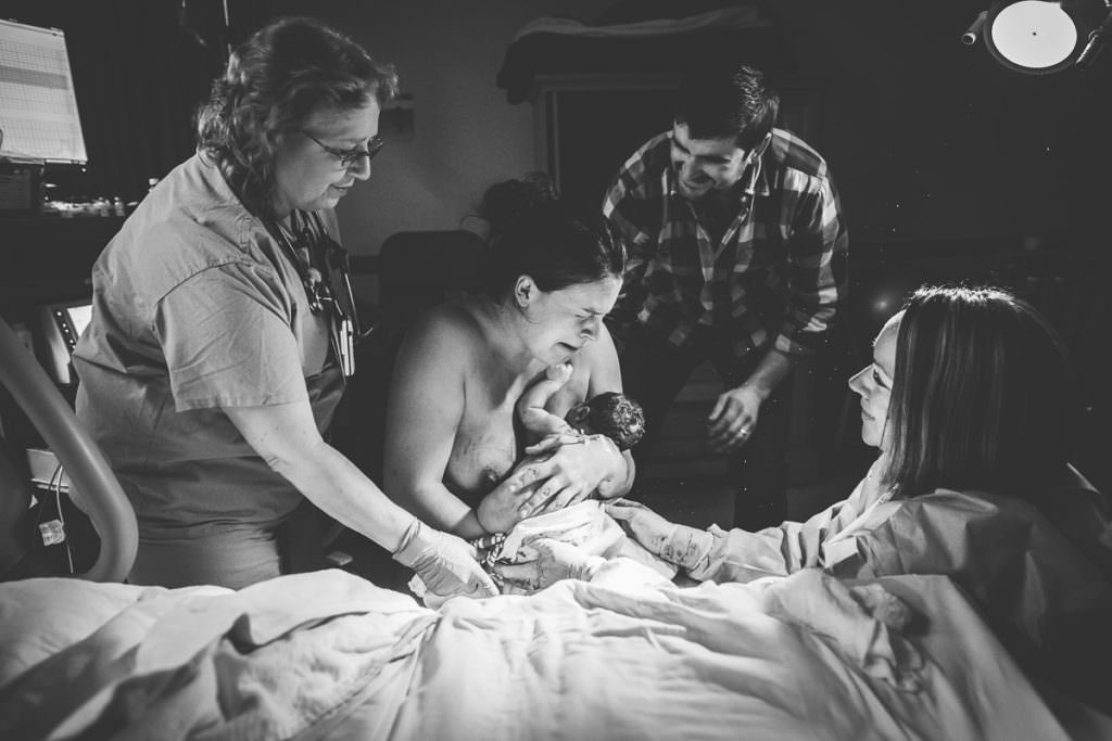 nurse midwife and husband all smile at mom who is crying with relief that she had her vbac birth