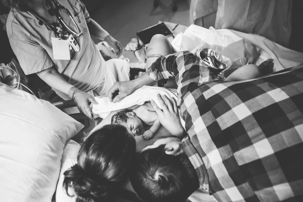 down view of mom and dad gazing down at baby while mom delivers placenta