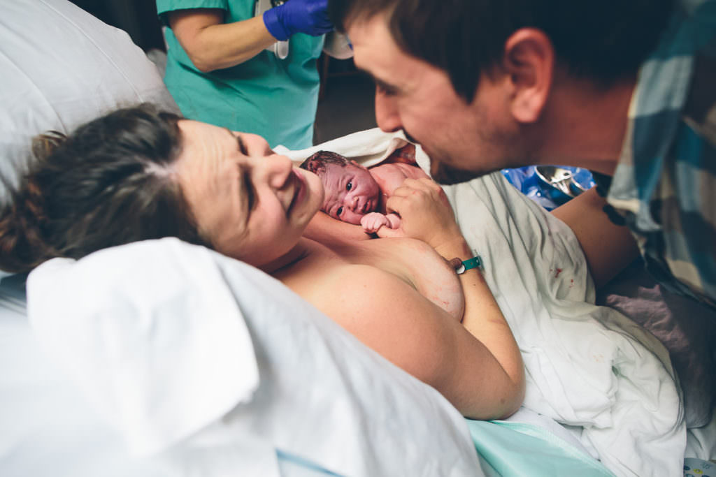 mom and dad looking at eachother but focus on newborn baby on chest