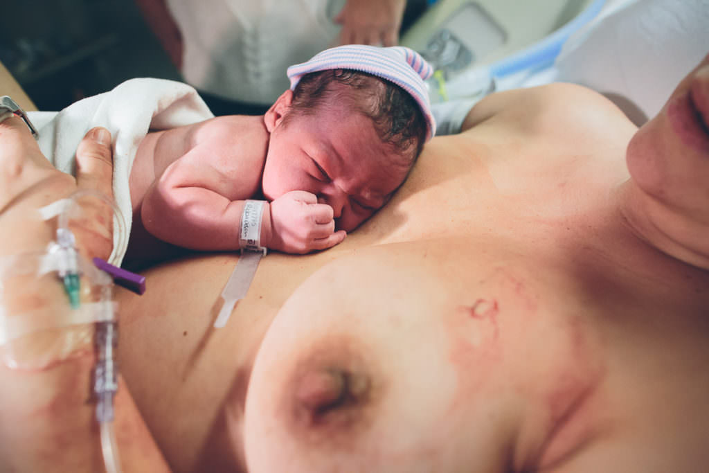baby laying on moms breast after he is born wearing a hospital hat