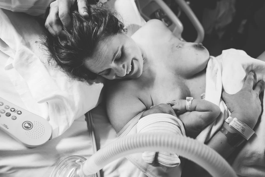 mom smiles down at newborn baby boy trying to nurse for the first time
