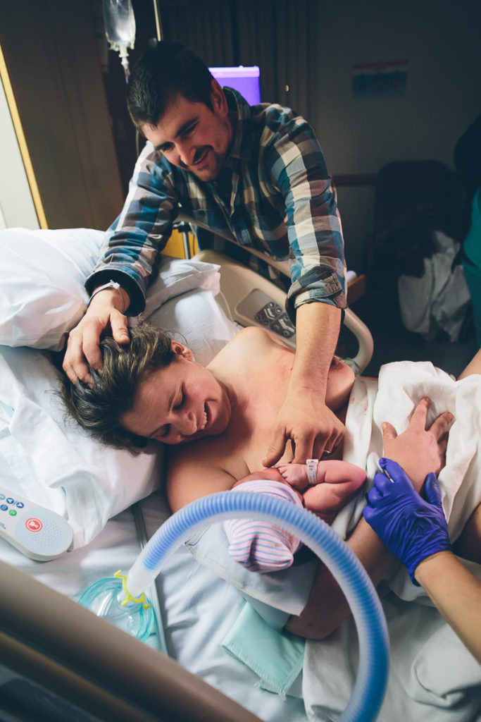 dad with hand on moms head gazing and holding hands with newborn baby boy