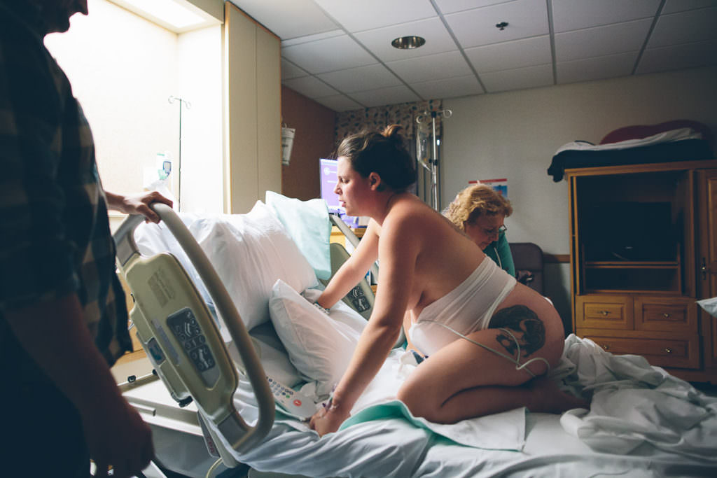 mom laboring on her knees wearing a belly monitor and tattoo on her leg