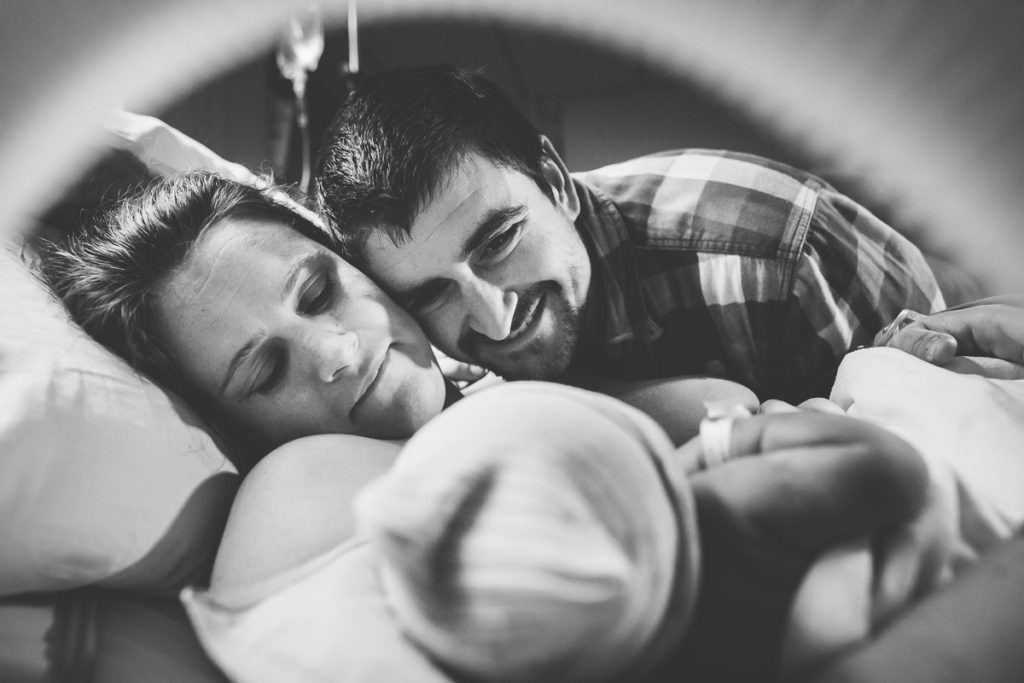 black and white mom and dad look at newborn baby wearing hospital hat