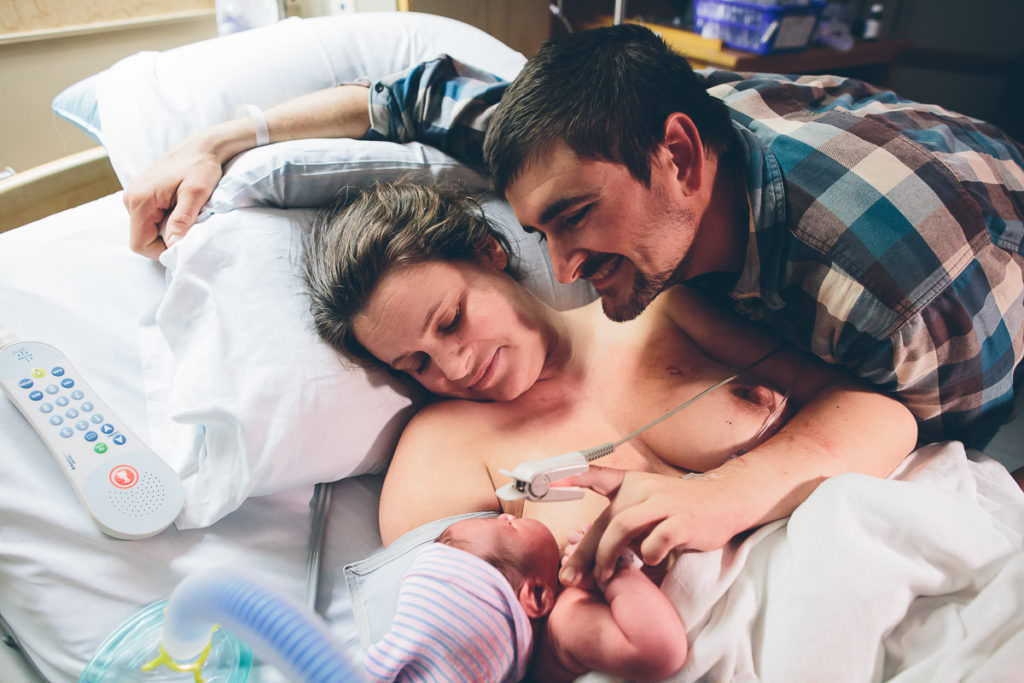 mom and dad laying on hospital bed looking at new baby after vbac