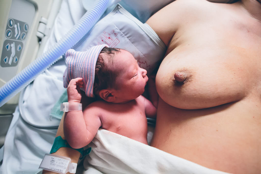 newborn baby with hospital hat falls asleep facing moms breast