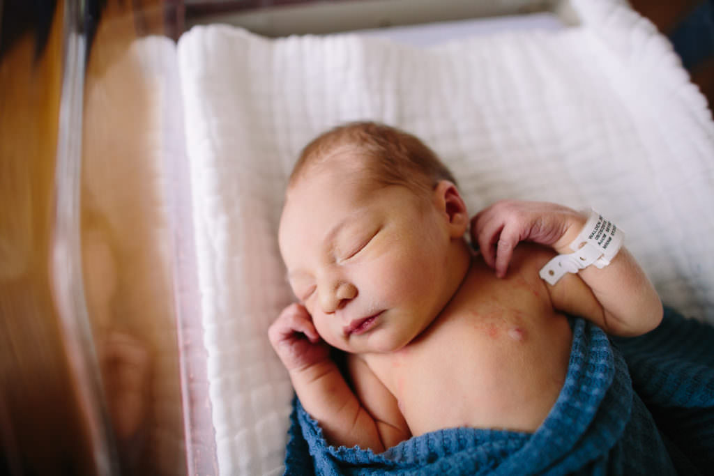 newborn baby boy sleeping in a bassinet and wrapped in blue blanket during fresh 48 session