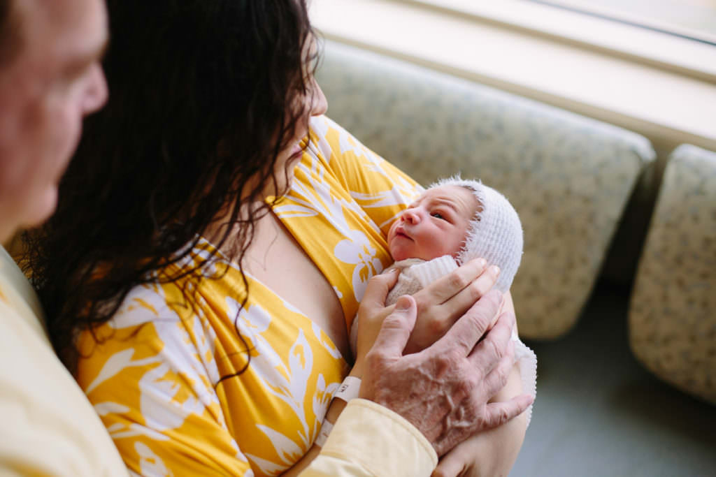 mom in yellow dress holding baby boy on hospital couch during fresh 48