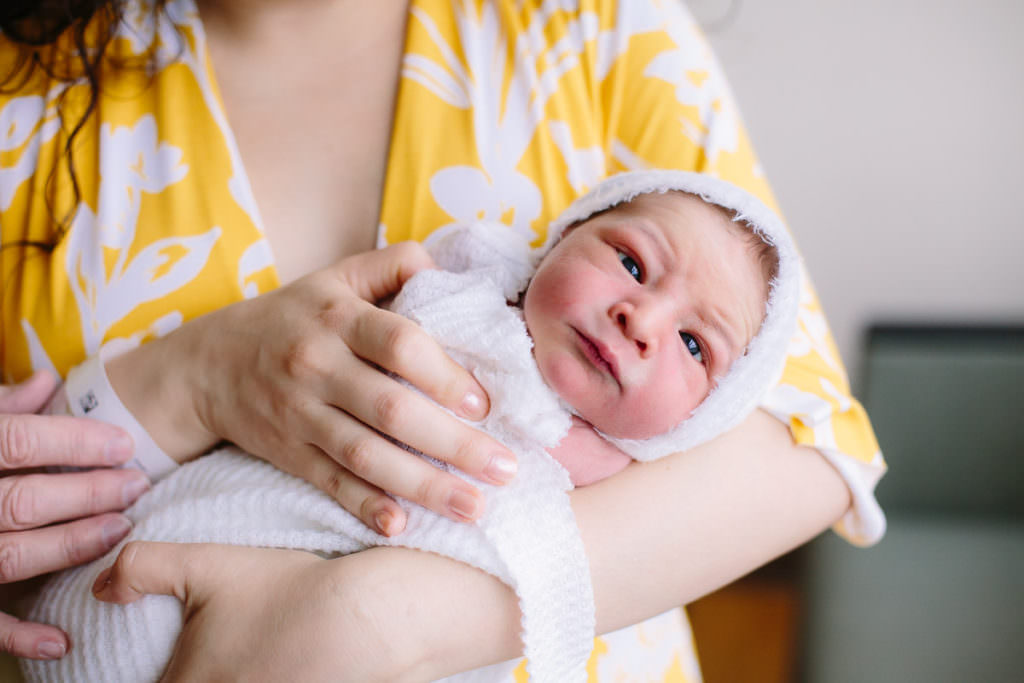 mom in yellow dress holding baby swaddled in white