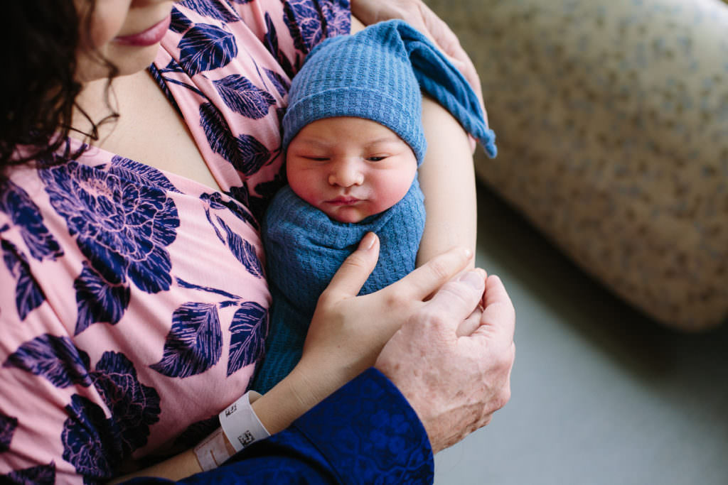 baby boy snuggling with mom wearing a long blue hat