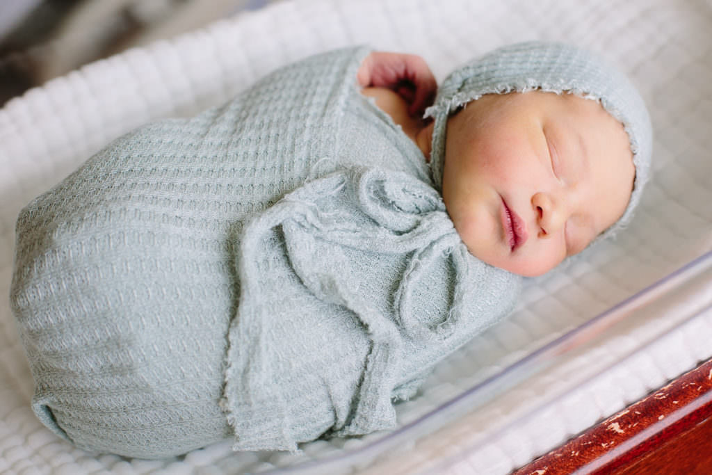 fresh new baby boy wrapped in blue laying in hospital bassinet