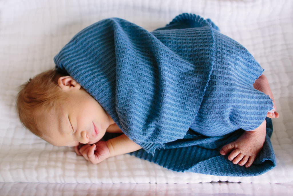 newborn baby laying in hospital bassinet with sleepy smile