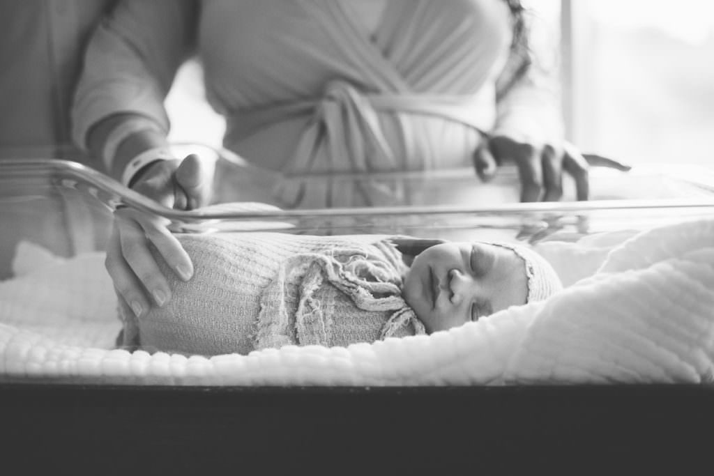 mom in robe puts arm on newborn baby laying in bassinet